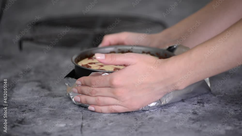 Woman preparing cheesecake with berry sauce in the kitchen. Wrapping the aluminum foil around the springform pan. Woman preparing cheesecake with berry sauce in the kitchen. Wrapping the aluminum foil around the springform pan.