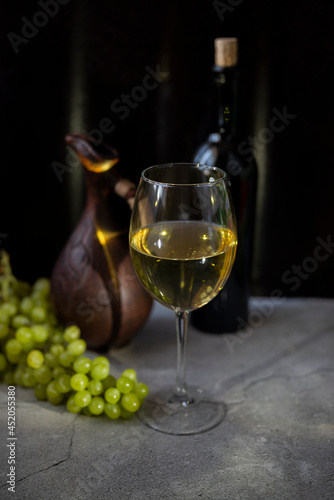 a glass of white wine with a grape bottle and a clay decanter