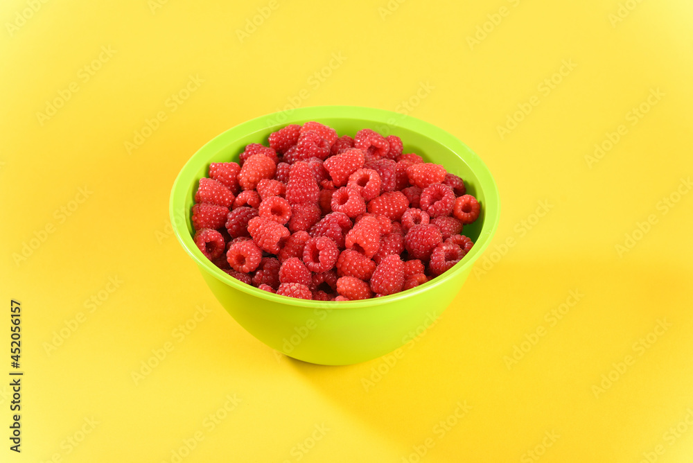Ripe raspberry in a green plate on yellow background. Ripe raspberry in a green plate on yellow background.