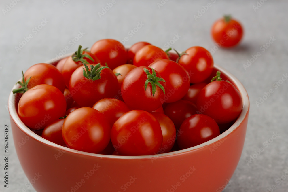 Cherry tomatoes in a red bowl on grey background Cherry tomatoes in a red bowl on grey background