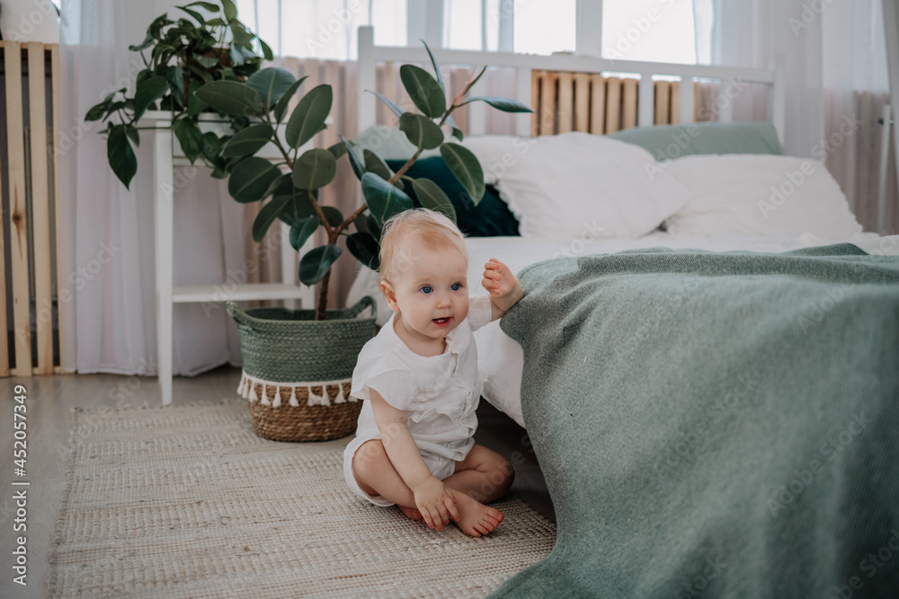 Naklejka premium a baby girl in a muslin jumpsuit is sitting on the floor on a rug in the bedroom