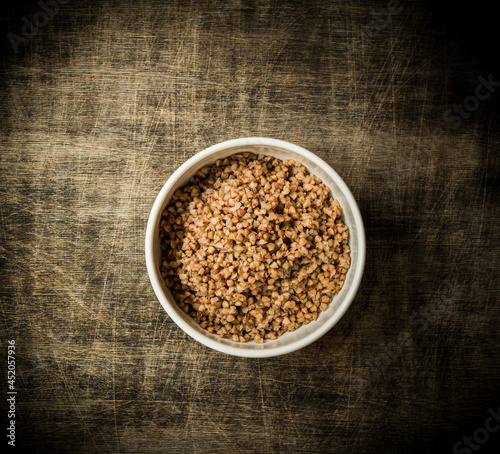 Buckwheat porridge in a white plate placed on a dark wooden background, close up
