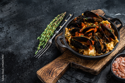 Mafaldine pasta with mussels and tomato sauce. Black background. Top view. Copy space
