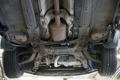Bottom view of the front of a modern car. Suspension parts, exhaust system, catalytic converter. Selected focus.