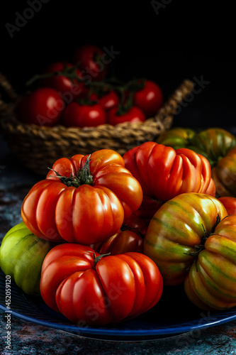 Raw fresh tomatoes on dark blue plate. Group of lined creasy organic Raf tomatos. Low key side view photo with soft focus.