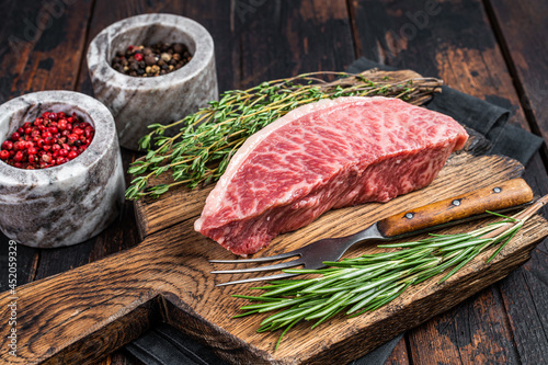 Wagyu A5 raw rump or sirloin steak, kobe beef meat on a butchery board. Dark wooden background. Top view photo