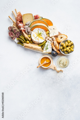 Assorted cheeses on wooden board plate, olive, grapes, bread on white background, top view, flat lay, copy space.