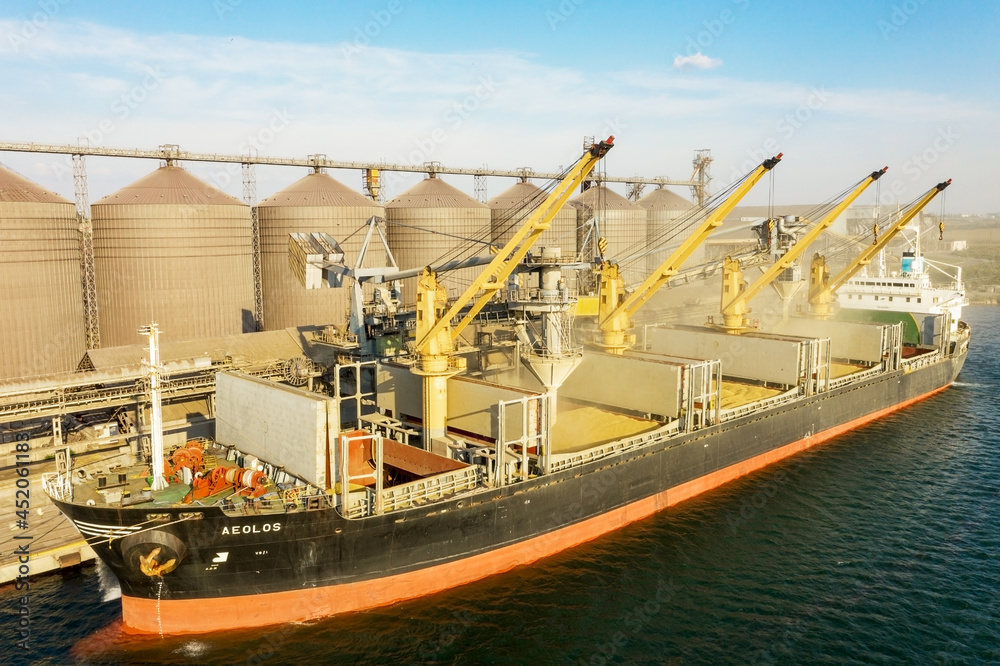 ODESSA, UKRAINE - August 9, 2021: Loading grain into holds of sea cargo vessel through an automatic line in seaport from silos of grain storage. Bunkering of dry cargo ship with grain - obrazy, fototapety, plakaty 