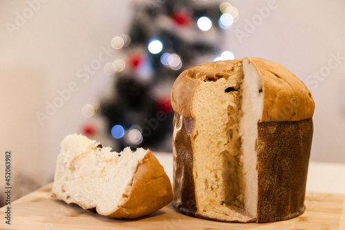 Panettone slice with Christmas tree
and blurry lights flashing in the background. Panettone concept. Christmas concept.