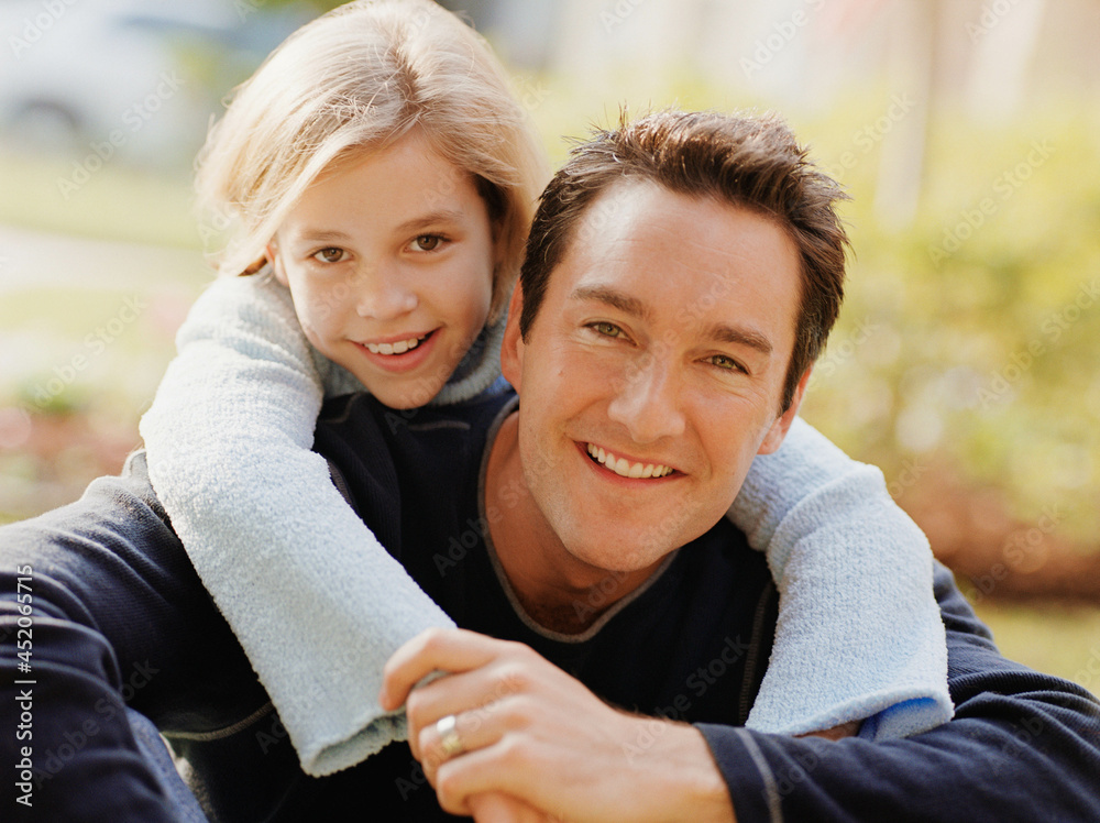 Daughter with arms wrapped around fathers shoulders sitting on front lawn of home Daughter with arms wrapped around fathers shoulders sitting on front lawn of home