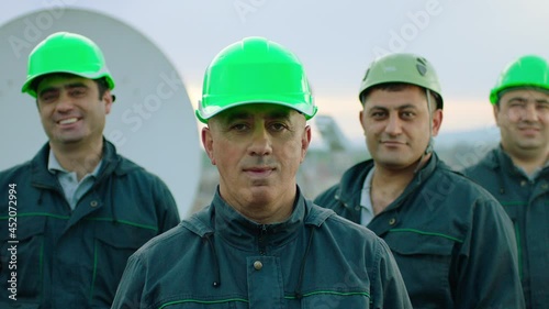 Wallpaper Mural Portrait of group of professional telecommunication industry engineers smiles and looks at the camera . Workers wearing safety uniform and hard hat on unfocused background with sky and antennas . Torontodigital.ca
