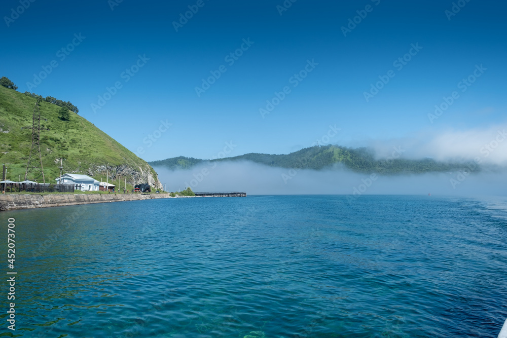 Lake Baikal close to village Port Baikal, Russia. Sunny day view of the high shore and clear lake water with fog Lake Baikal close to village Port Baikal, Russia. Sunny day view of the high shore and clear lake water with fog