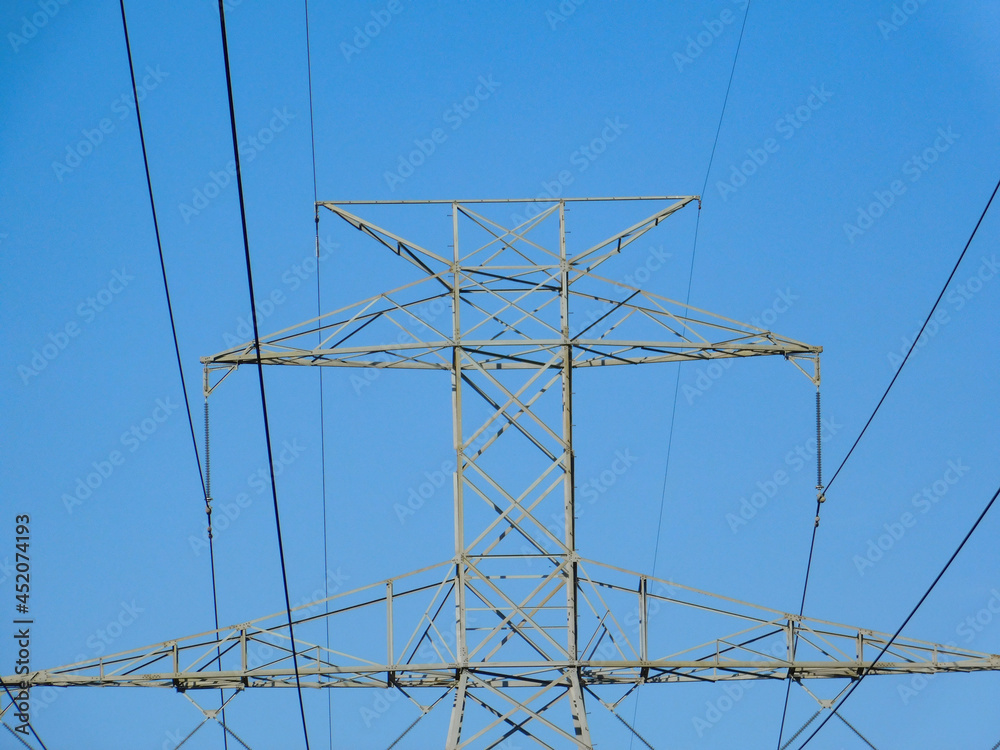 Centered top of Powerline Tower with powerlines against clear sky in direct evening sunlight. Centered top of Powerline Tower with powerlines against clear sky in direct evening sunlight.