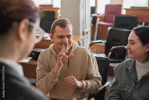 Two girls and a guy are talking in sign language. Three deaf students chatting in a university classroom.