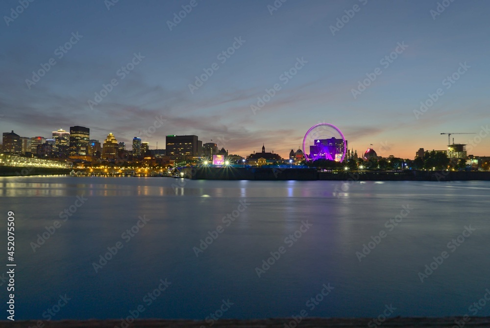 A skyline of Montreal Old Port and Downtown at the twilight blue hour. Foreground is Saint Lawrence (Laurent) river.