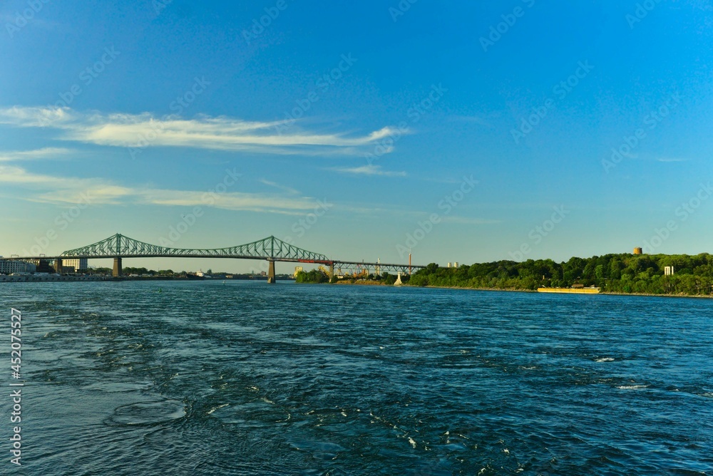 A skyline view a steel bridge across a river on bright sunny summer day. Jacques Cartier Bridge across Saint Lawrence (Laurent) river, Montreal, Quebec, Canada