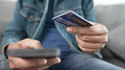 A middle-aged Asian man holding credit card for shopping payment online with smartphome sitting in living room at home. photo