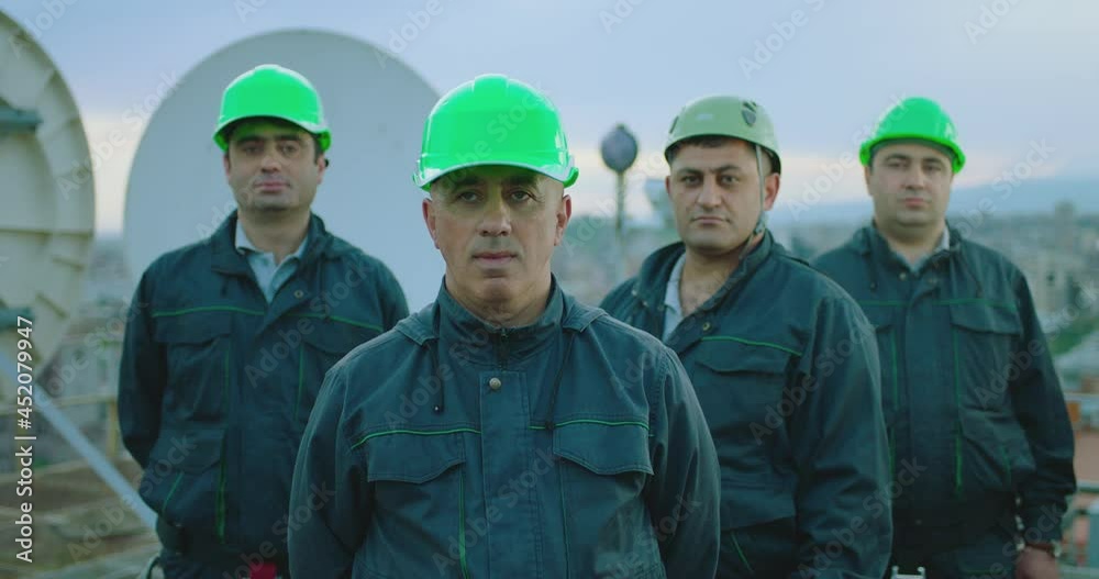 Portrait of group of professional telecommunication industry engineers smiles and looks at the camera . Workers wearing safety uniform and hard hat on unfocused background with sky and antennas . Portrait of group of professional telecommunication industry engineers smiles and looks at the camera . Workers wearing safety uniform and hard hat on unfocused background with sky and antennas .