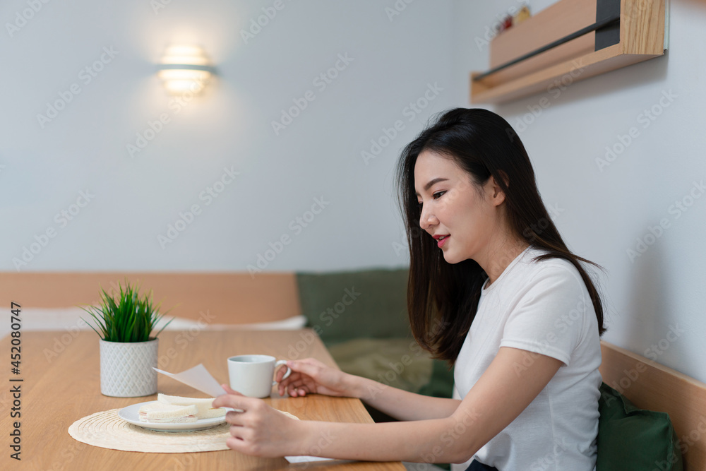 Living room concept a pretty lady reading the article on the paper while another hand holding a cup of caffeine beverage in the morning Living room concept a pretty lady reading the article on the paper while another hand holding a cup of caffeine beverage in the morning