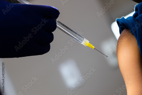 Dark hand of doctor administering vaccination shot with needle and young patient's arm.