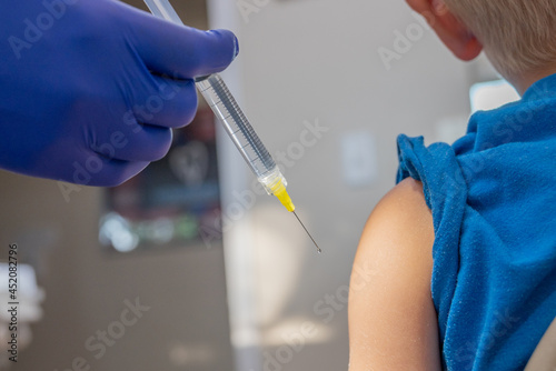 Young child getting vaccination shot in shoulder with doctor's hands in blue gloves