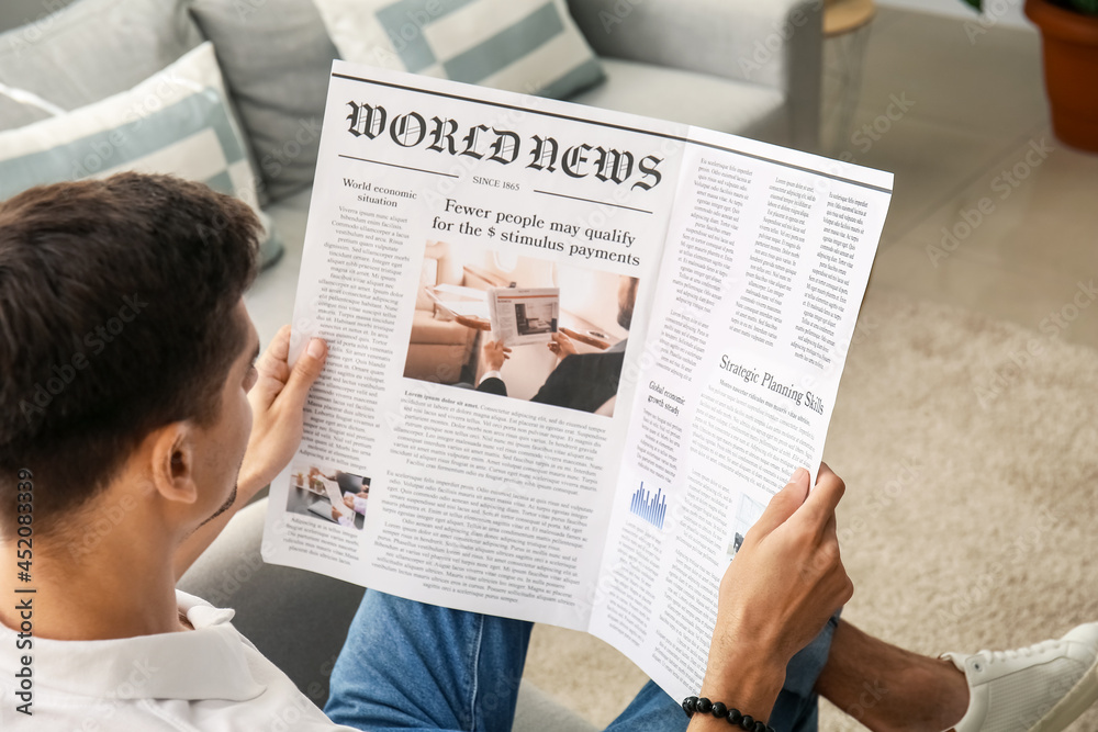 Naklejka premium Young man reading newspaper at home