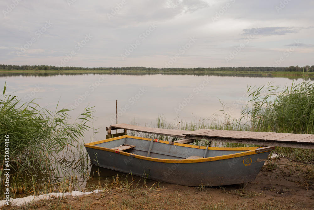 A gray boat stands on the shore of the lake next to a wooden bridge in cloudy weather.