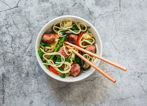 Noodles with meatballs and vegetables cauliflower, zucchini, pepper, spinach, eggplant, carrot fried wok on a grey  background, top view