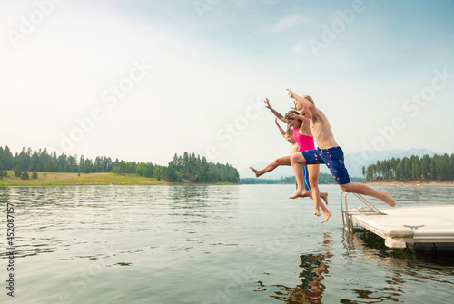Group of kids jumping off the dock into the lake together during a fun summer vacation. 
