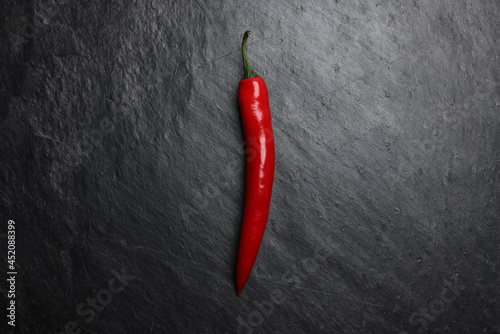 Red hot chilli pepper on dark black rough slate stone surface background