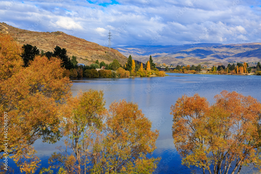 A deep blue lake surrounded by autumn trees. Photographed at Lake Dunstan, Cromwell, New Zealand