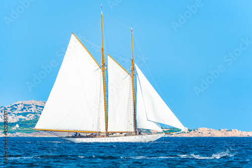 Stunning view of a wooden sailboat with white sails sailing on a blue water during a sunny day. Isola di Spargi, Maddalena Archipelago, Costa Smeralda, Sardinia, Italy.