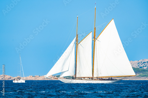 Stunning view of a wooden sailboat with white sails sailing on a blue water during a sunny day. Isola di Spargi, Maddalena Archipelago, Costa Smeralda, Sardinia, Italy.