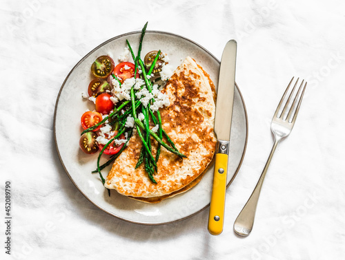 Oatmeal crepes without flour with asparagus, feta, cherry tomatoes - delicious diet breakfast on a dark background, top view