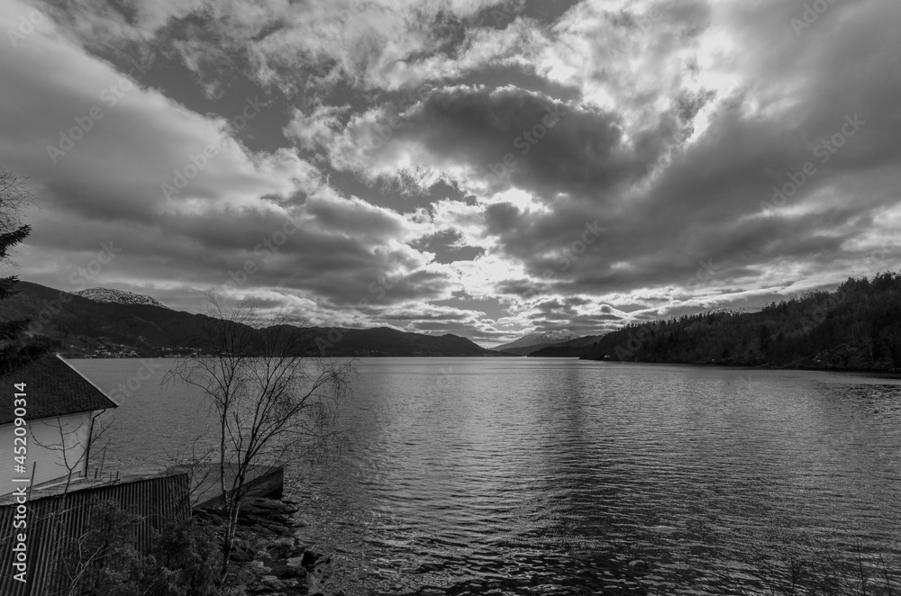 Black and white of a fjord surrounded by hills with mountains in the distance. 