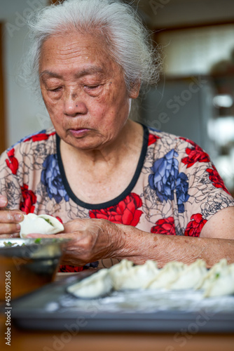 An old grandmother in a Chinese family is making dumplings