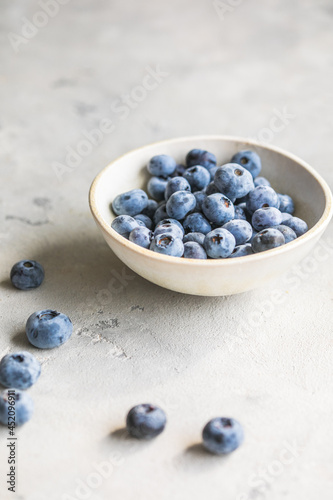 Freshly picked blueberries in a bowl. Juicy and fresh berries with green leaves on a rustic table. Healthy food and nutrition concept