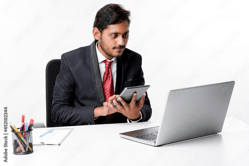 Young indian man in suit and using tablet and laptop at office
