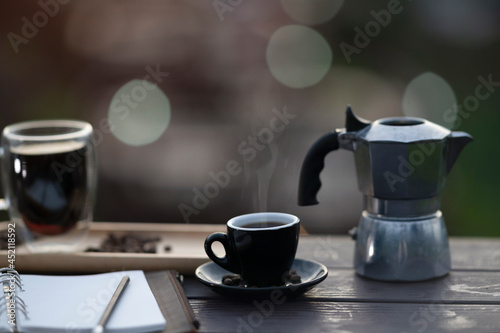 Closed up with a hot coffee, moka pot and note papers place on the wooden table with bokeh background.
