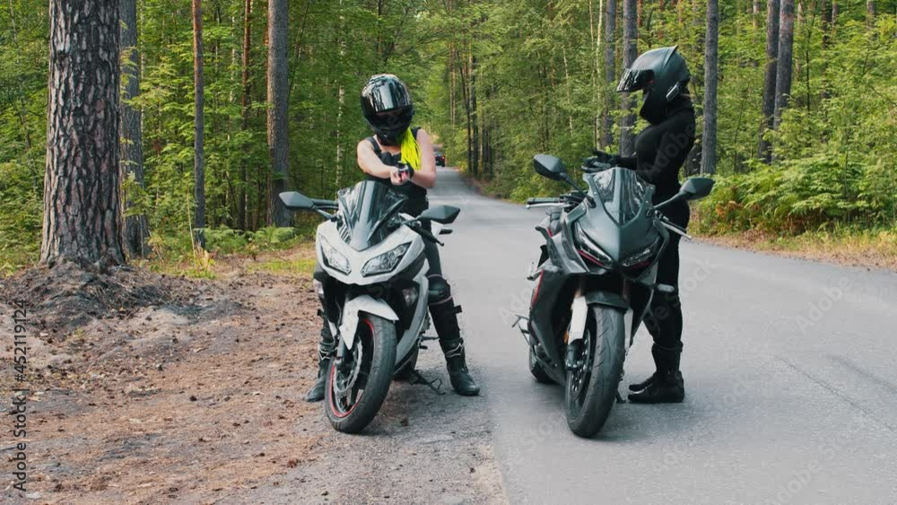 Women friends stands up from the motorbikes in the forest Women friends stands up from the motorbikes in the forest