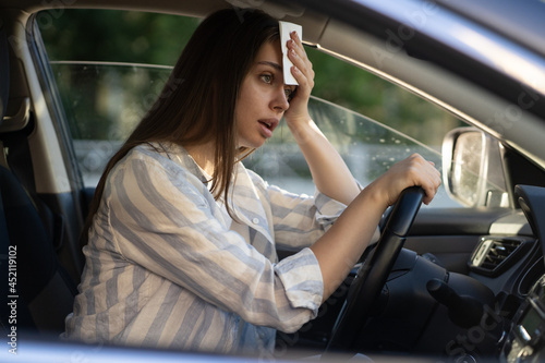 Foto Girl driver being hot during heat wave in car, suffering from hot weather, has problem with a non-working air conditioner, wipes sweat from her forehead with tissue