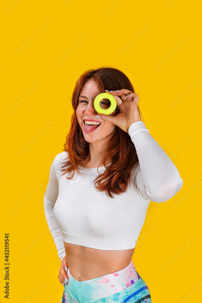 Fitness trainer shows exercises. A beautiful sports girl is engaged with rubber expander. Smiling fitness model in sportswear on yellow background. Advertising for the sports hall. Healthy lifestyle Fitness trainer shows exercises. A beautiful sports girl is engaged with rubber expander. Smiling fitness model in sportswear on yellow background. Advertising for the sports hall. Healthy lifestyle