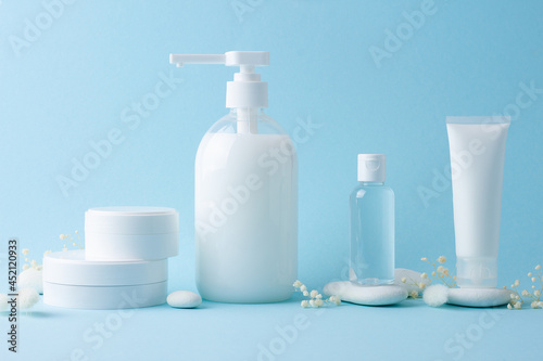 Cosmetic skin care products with flowers and stones on blue background. Close up