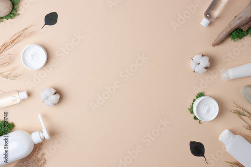 Cosmetic skin care products with flowers and wood on pastel beige background. Flat lay, copy space