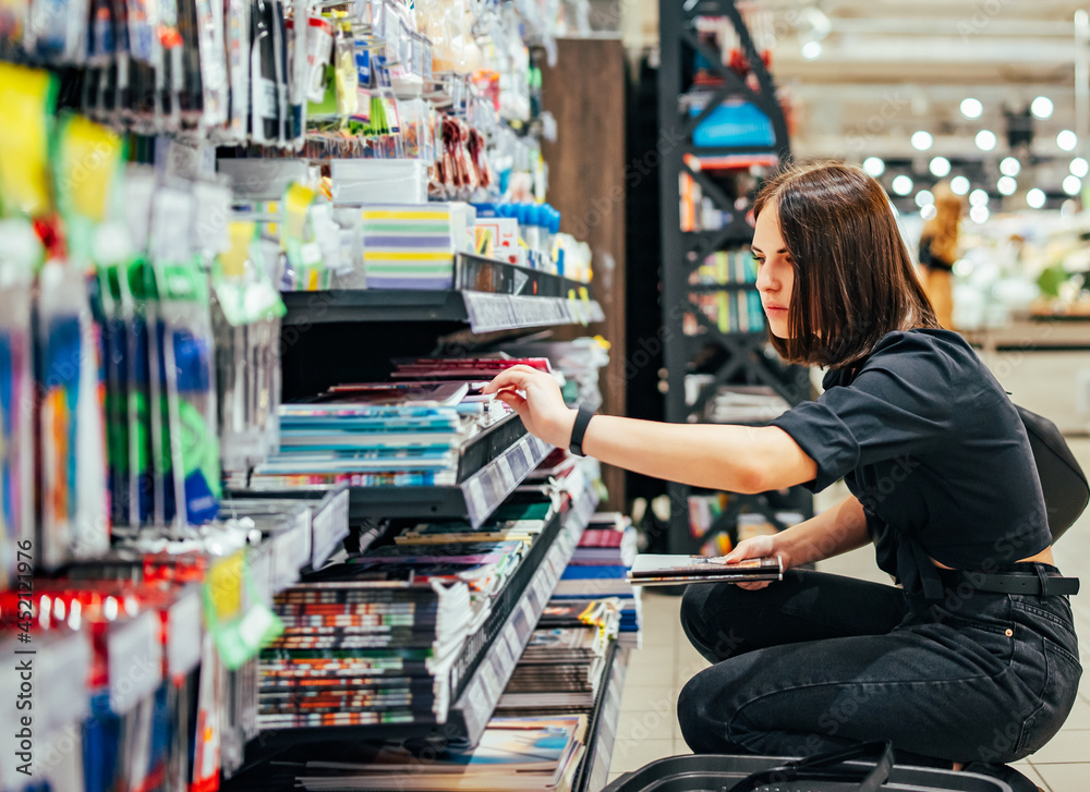 Portrait of young woman choosing school stationery in supermarket.