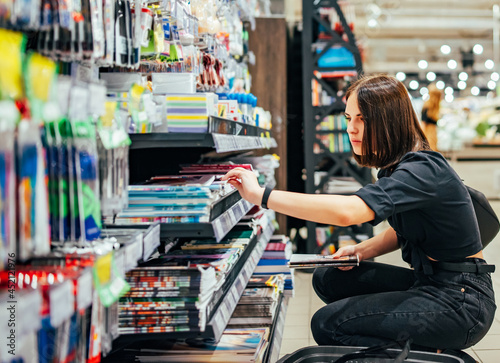 Portrait of young woman choosing school stationery in supermarket.