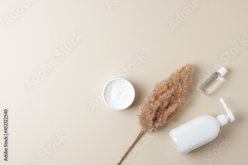Cosmetic skin care products with pampas on pastel beige background. Flat lay, copy space