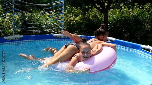 Happy girls have fun floating together on swim ring in outdoor swimming pool, summer