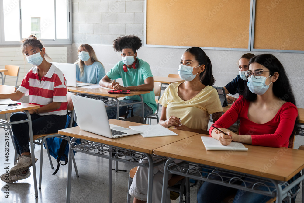 Group of multiracial teen highschool students wearing face mask listen to teacher lesson.