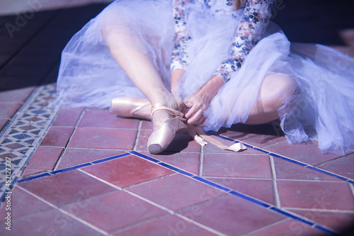 Detail of hands of female classical ballet dancer sitting on the floor putting on her slippers, wearing a white tutu.